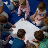 Students and children gathered in a circle working on an activity